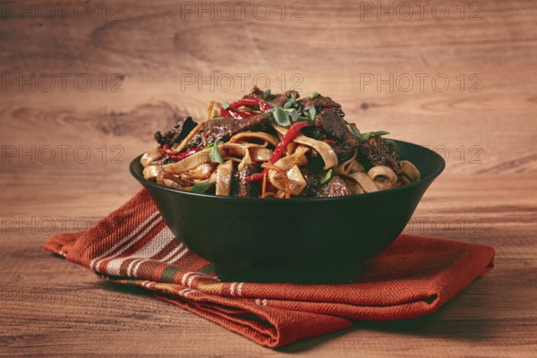 Udon noodles with beef in Mongolian style, with green onions and vegetables, served in a black bowl, on a wooden table, homemade, no people