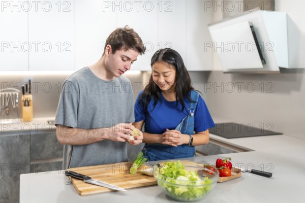 Multiethnic couple joyfully preparing a vibrant, healthy salad together in their modern kitchen, surrounded by fresh ingredients and love
