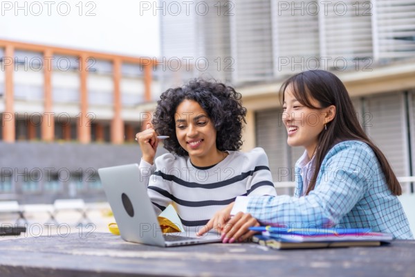 Happy multi-ethnic female students using laptop sitting on the campus