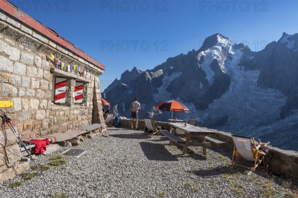 Moutain hut Cabane de l'A Neuve, tourists sitting on terrace, Aiguille Rouges du Dolent massif at back, near La Fouly, Val de Ferret, Switzerland, Europe