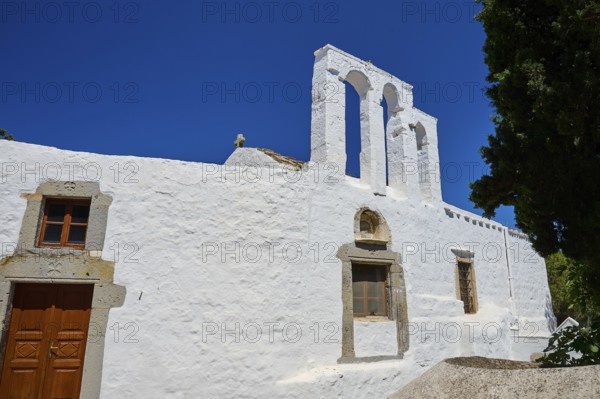 White church with bell tower and wooden door in front of a bright blue sky, Chora, Old Town, Patmos, Dodecanese, Greek Islands, Greece, Europe