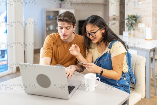 Multiethnic couple making online purchases using laptop and credit card, enjoying a convenient and secure shopping experience from home