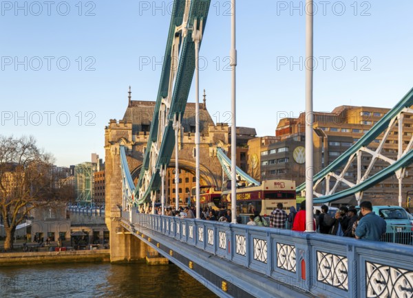 People and open top tour buses cross Tower Bridge in late afternoon, London, England, UK