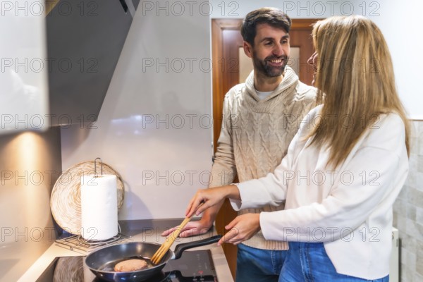 Happy couple preparing dinner together, cooking meat in a pan on the stovetop in their modern kitchen