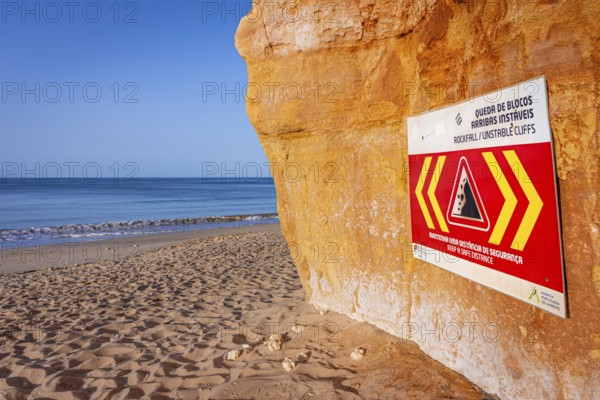 ROCKFALL UNSTABLE CLIFFS, KEEP A SAFE DISTANCE is written in English on a warning sign in Portugal on the cliffs of the Atlantic Ocean. Rocks and stones break out here again and again and injure people., Albufeira, Faro, Portugal, Europe