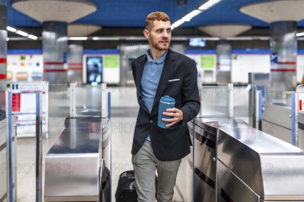 Young professional walking through subway turnstile holding reusable coffee cup, commuting to work in the morning
