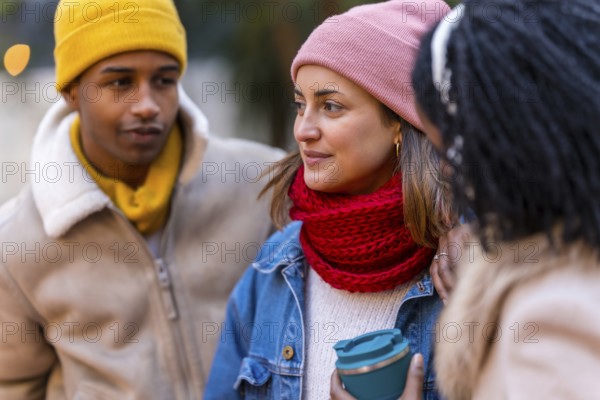 Three friends are chatting and laughing together on a cold winter day in the city, enjoying each other's company and the festive atmosphere