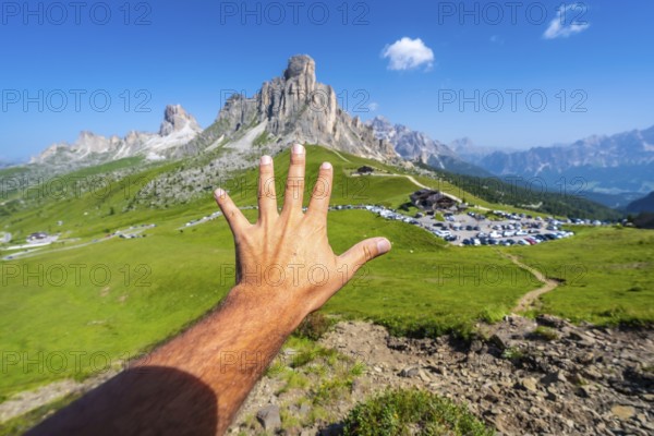 Male tourist showing five fingers with the majestic nuvolau peak and the passo giau mountain pass in the background on a sunny summer day