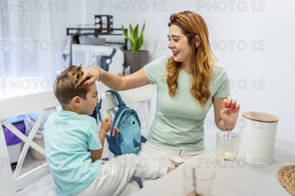 Tender caucasian mother sitting on the kitchen stroking her son's head before he goes to school