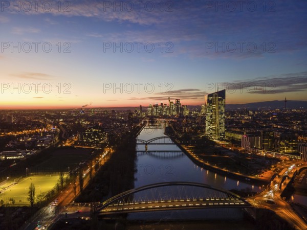 The lights in the offices of the European Central Bank (ECB) and in the skyscrapers of Frankfurt's banking skyline glow in the evening shortly after sunset. (Aerial view with a drone), Frankfurt am Main, Osthafen, Hesse, Germany, Europe