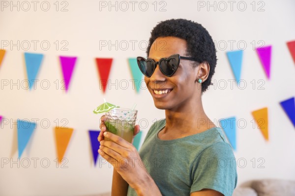 Portrait of a happy latin man with sunglasses drinking cocktail next to garlands decorating a house during celebration