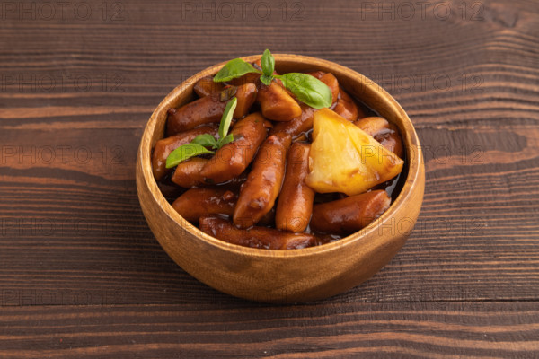 Tteokbokki or Topokki, fried rice cake stick, popular Korean street food with spicy jjajang sauce and pineapple on brown wooden background. Side view