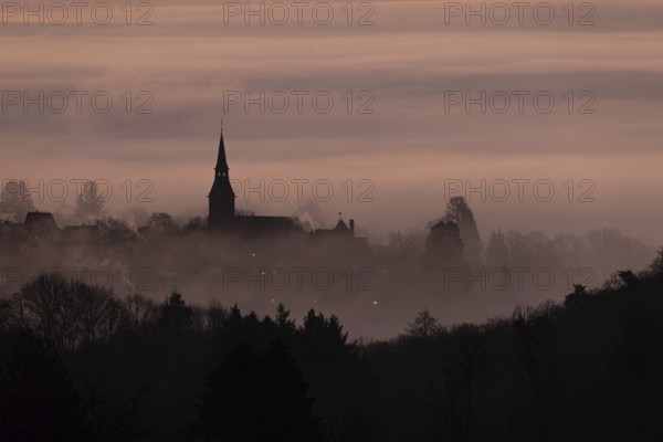 Wisps of mist drift into the town of Kronberg im Taunus in the morning shortly in front of sunrise. Only the spire of St Peter and Paul's Church stands out. Kronberg, Malerblick, Hesse, Germany, Europe