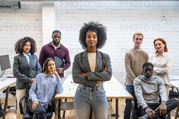 Confident african woman standing with arms crossed next to colleagues in a coworking