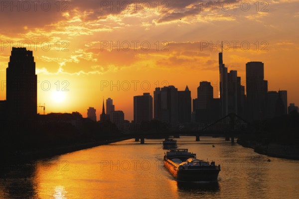 The sun sets behind the Frankfurt bank skyline while a ship sails along the Main, Frankfurt am Main, Hesse, Germany, Europe