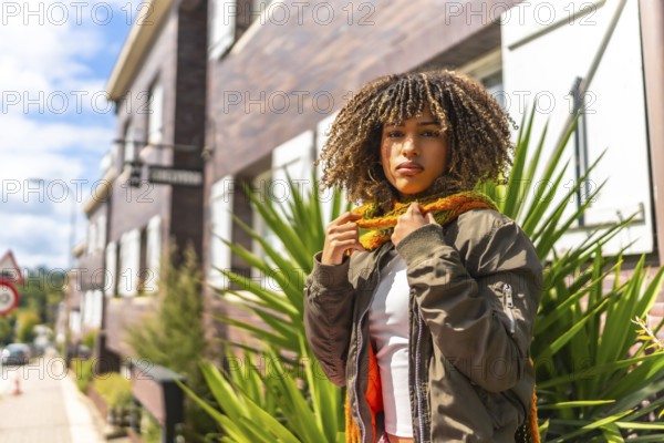 Latin woman in warm clothes standing outside a house in the street in a sunny day