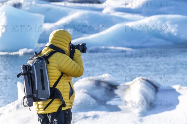 A photographer photographing the floating icebergs in the Jokulsarlon glacier lagoon in Iceland. Wearing a yellow winter jacket