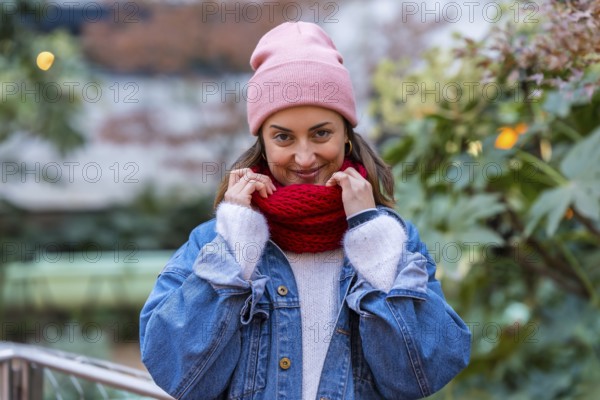 Young woman enjoying a winter day in the city, wearing a cozy pink beanie and a vibrant red scarf, radiating happiness and style