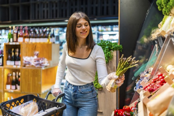 Young woman shopping for fresh asparagus in a supermarket, highlighting healthy eating habits and the selection of quality produce