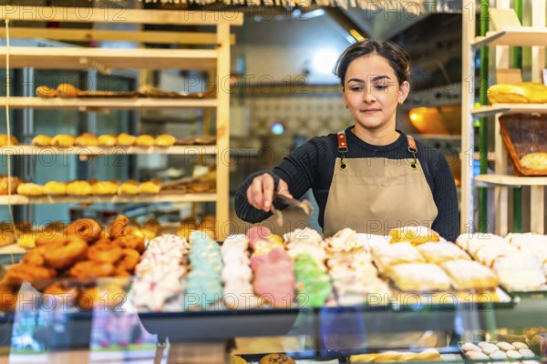 Latin young woman wearing apron selling artisan pastries in a bakery