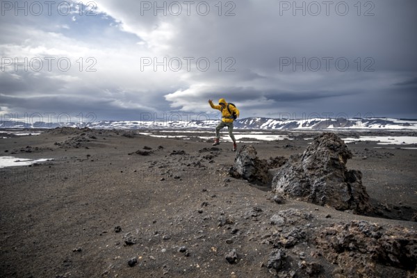 Hiker jumps into the air, snow-covered volcanic landscape with volcanic sand and petrified lava, crater of Askja volcano, Icelandic highlands, Iceland, Europe