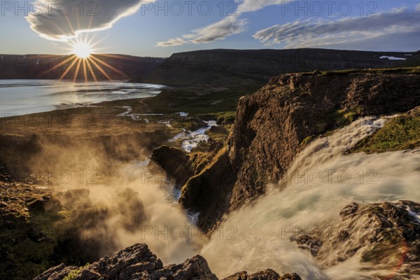 Waterfall backlit by midnight sun in front of mountains and coast, summer, Dynjandi, Westfjords, Iceland, Europe