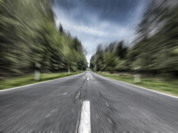 Photo with speed effect high speed speeding without speed limit from country road with central reservation leading to long straight ahead through mixed forest wooded area, Germany, Europe