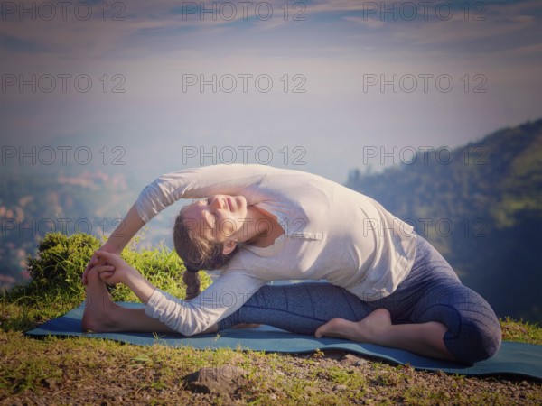 Yoga outdoors, young sporty fit woman doing Hatha Yoga asana parivritta janu sirsasana, Revolved Head-to-Knee Pose, in mountains in the morning. Vintage retro effect filtered hipster style image