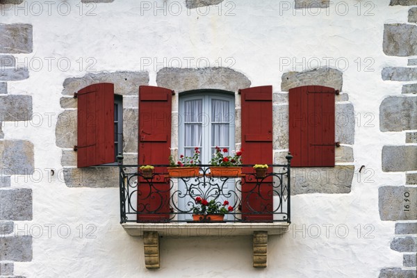 Typical window with balcony, red shutters and potted plants, detail of the façade, Espelette, Département Pyrénées-Atlantiques. Region Nouvelle-Aquitaine, Pays Basque, Basque Country, France, Europe