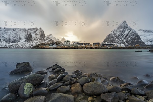 Traditional yellow rorbuer cabins on Sakrisøy Island, snow-capped rocky mountains in the back, Sakrisoy, Reine, Lofoten, Norway, Europe
