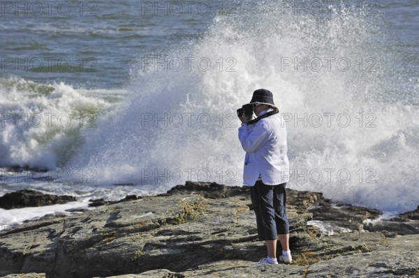 Tourist taking pictures of waves crashing on the rocks at the Pointe Saint-Gildas, Saint Gildas Point, Loire-Atlantique, France, Europe
