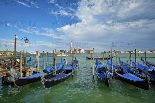 VENICE, ITALY, JUNE 27, 2018: Gondolas and gondolier in lagoon of Venice by Saint Mark (San Marco) square with San Giorgio di Maggiore church in background in Venice, Italy, Europe