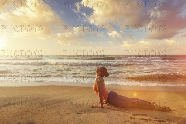 Yoga outdoors on beach, woman practices Ashtanga Vinyasa yoga Surya Namaskar Sun Salutation asana Urdhva Mukha Svanasana, upward facing dog pose on sunset. With light leak and lens flare
