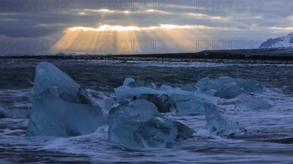 Waves breaking on icebergs on the black beach of Breidamerkursandur, sunset, near Jökullsarlon, Sudurland, Iceland, Europe