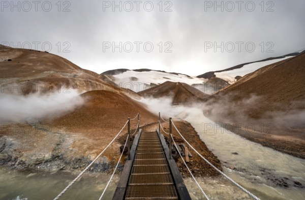 Bridge over steaming stream between colourful rhyolite mountains with snowfields, Hveradalir geothermal area, Kerlingarfjöll, Icelandic highlands, Iceland, Europe