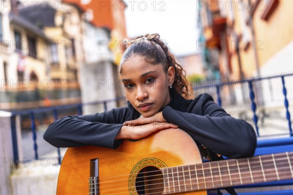 Portrait of a beauty african american woman leaning on an acoustic guitar outside a colorful building