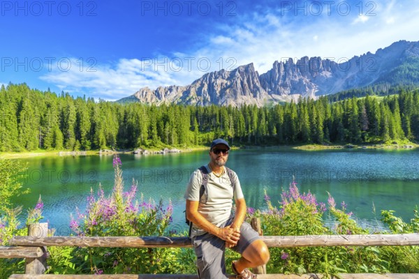Hiker enjoying the breathtaking view of the emerald waters of lake carezza and the latemar massif in the italian dolomites
