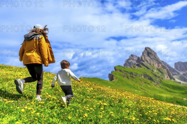 Tourists running on a flowery meadow with the odle and seceda mountains in the background, dolomites, italy