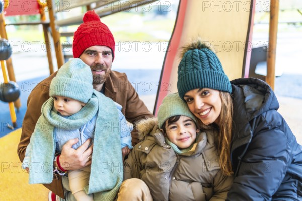Happy family bundled in winter clothing, smiling and embracing joyfully while enjoying playful moments together at the playground