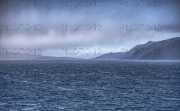 View of Cape Horn in the haze under a dramatic sky with distant coastlines, Chile, South America
