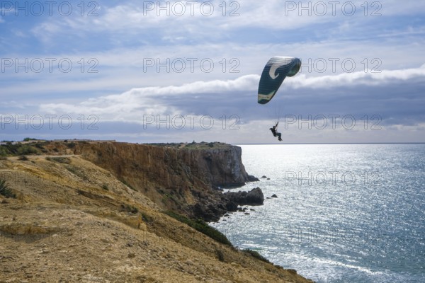 Sagres, Algarve, Portugal - Paraglider flying on the town beach Praia da Mareta, at the back left the viewpoint Ponta da Atalaia