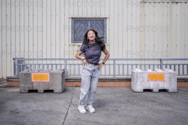 Female asian young K-pop dancer jumping hand on hip performing a choreography in an urban industrial space in the city