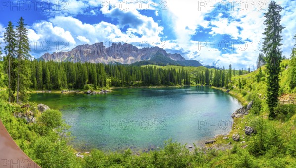Emerald green water of lake carezza reflecting latemar mountain range in italian dolomites, surrounded by coniferous forest on a sunny summer day