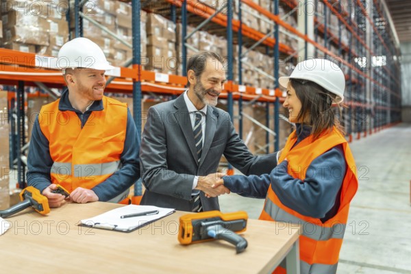Manager shaking hands with a smiling female worker in a logistics warehouse, a male worker is looking at them, barcode readers and contract on the table