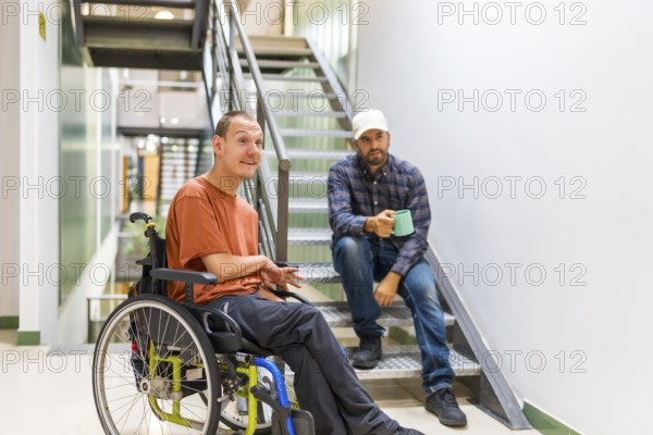 Man with cerebral palsy talking with a work colleague indoors in a modern coworking with staircase