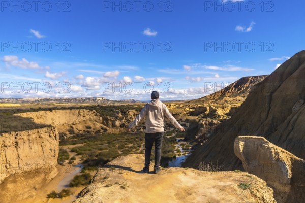 Tourist standing on a cliff with open arms, contemplating the breathtaking view of bardenas reales desert in navarre, spain, on a sunny day