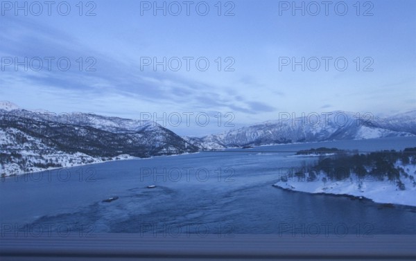 View of a river surrounded by snowy mountains under a clear blue sky, Norway, Europe