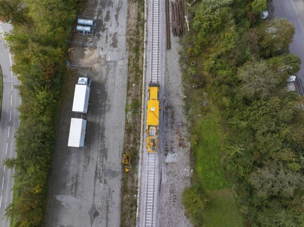 Top view of a yellow construction machine on a railway track next to a road and a storage yard, tamping machine, Hermann Hessebahn, Althengstett, Black Forest, Germany, Europe