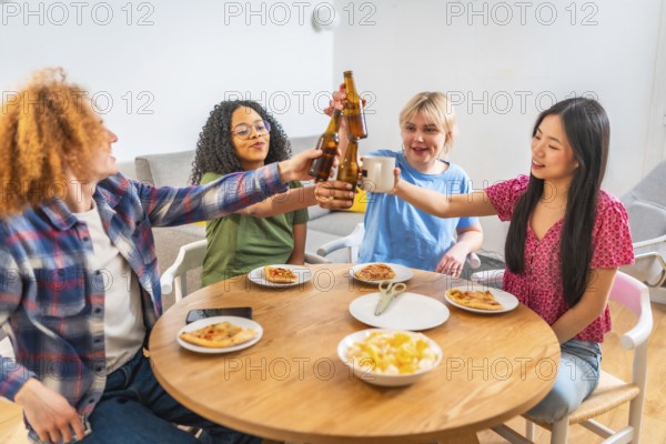 Four diverse friends are enjoying a meal together, toasting drinks and eating pizza at a round wooden table