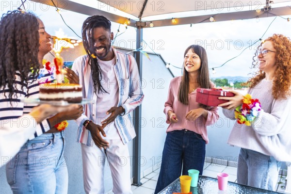 African happy woman receiving a gift and birthday cake celebrating with multi-ethnic friends in a terrace